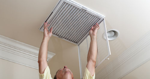 man changing AC filter on ceiling