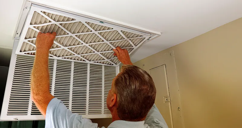 Man changing air filter on ceiling
