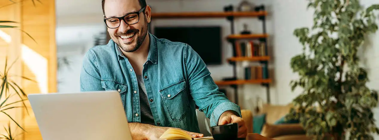 Man at home using his laptop and drinking coffee