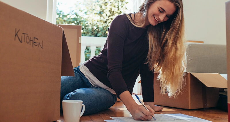 smiling-woman-sitting-with-moving-boxes-on-the-floor-making-a-list