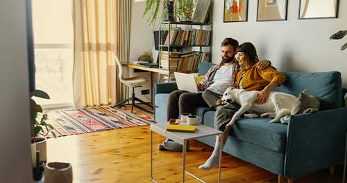 couple sitting on couch with laptop and dog