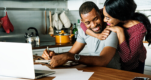 Happy couple paying bills at kitchen table