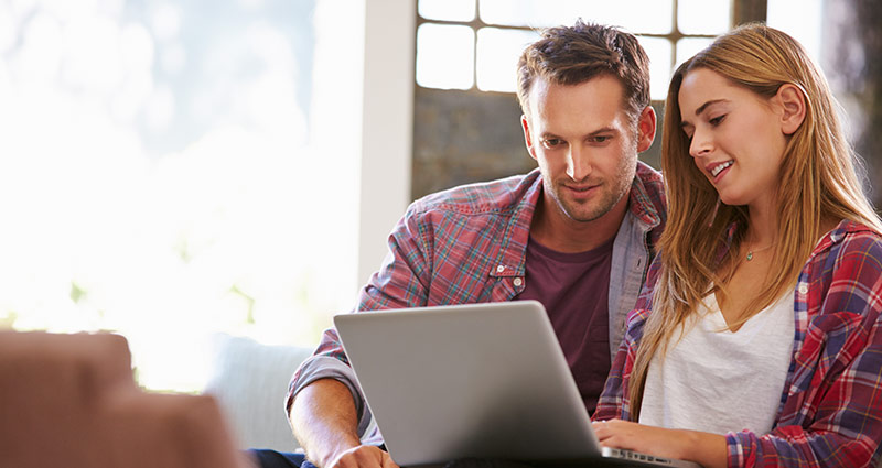 Photo of a couple sitting at a laptop looking at the sceen