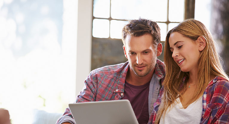 Photo of a couple sitting at a laptop looking at the sceen