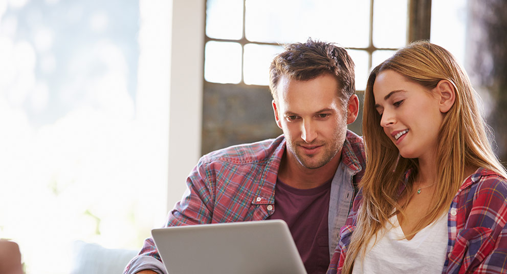 Photo of a couple sitting at a laptop looking at the sceen