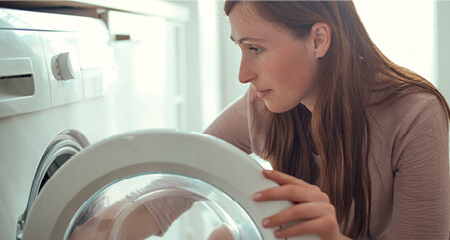 Photo of a woman loading  an eletric clothes dryer with clothing
