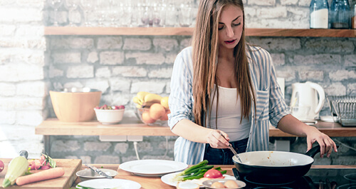 Young woman cooking a healthy meal on electric stove top