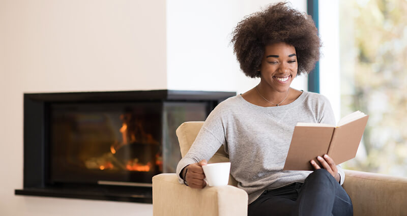 Black woman reading book in front of a fireplace