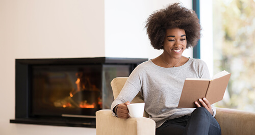 Black woman reading book in front of a fireplace