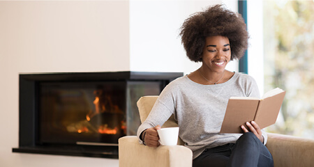 Black woman reading book in front of a fireplace