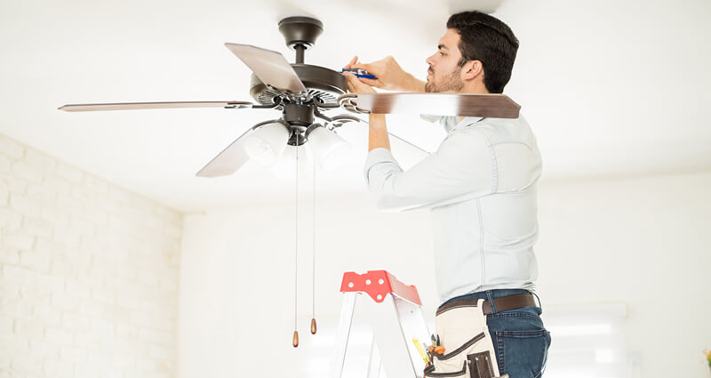 Man on a step ladder installing a ceiling fan