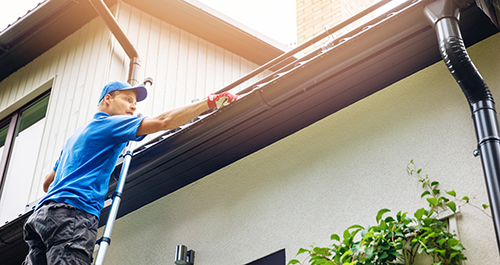 Man on a ladder inspecting his roof and rain gutters