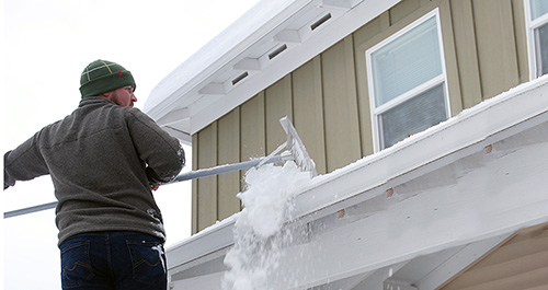 Man scraping ice and snow from his home's roof and windows