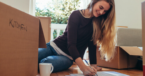 Smiling woman sitting with moving boxes on the floor making a list