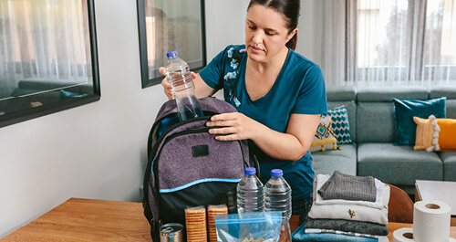 woman putting cans of food to prepare emergency backpack in living room