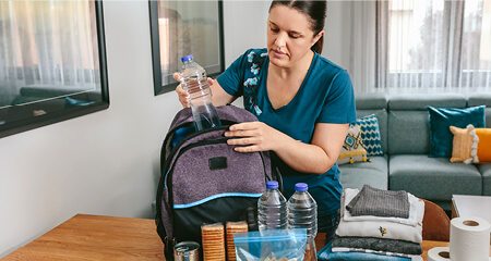 woman putting cans of food to prepare emergency backpack in living room