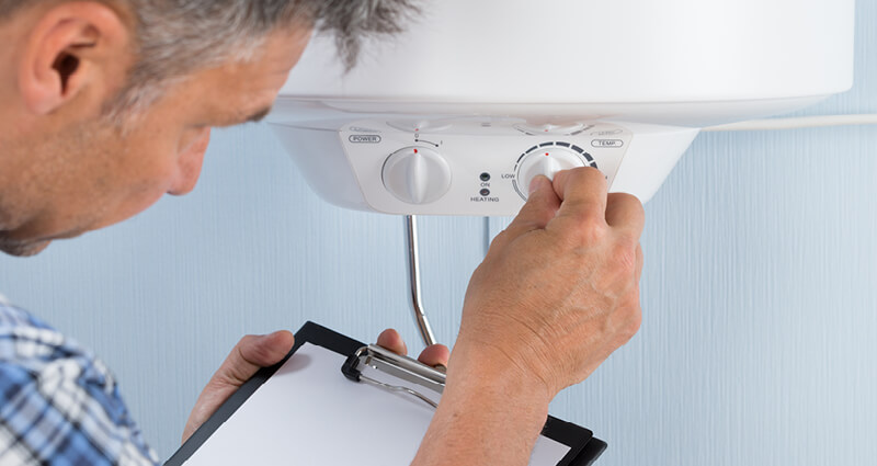 Plumber holding clipboard adjusting temperature of electric boiler