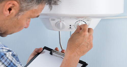 Plumber holding clipboard adjusting temperature of electric boiler
