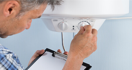 Plumber holding clipboard adjusting temperature of electric boiler