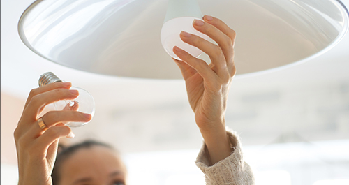 Woman changing out a traditional watt lightbulb for an LED bulb