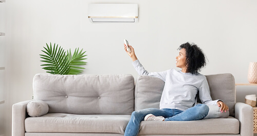 Woman sitting on couch pointing remote control at AC