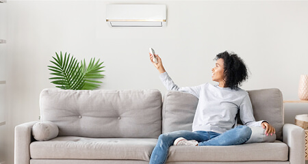 Woman sitting on couch pointing remote control at AC