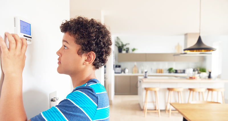 Boy changes temperature on central heating thermostat control