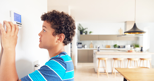 Boy changes temperature on central heating thermostat control