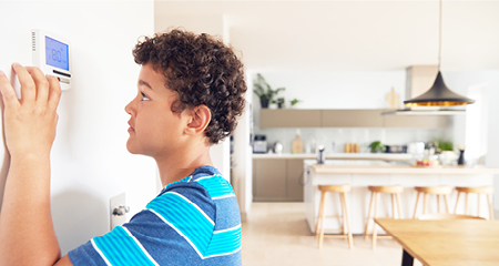 Boy changes temperature on central heating thermostat control